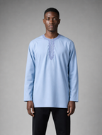 Men's light blue long sleeve short kurta with round embroidered neckline worn with black pants.